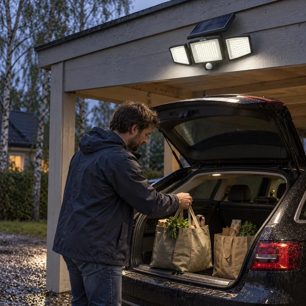 A man unloads shopping bags from his car under a lit Orvo solar light in a carport